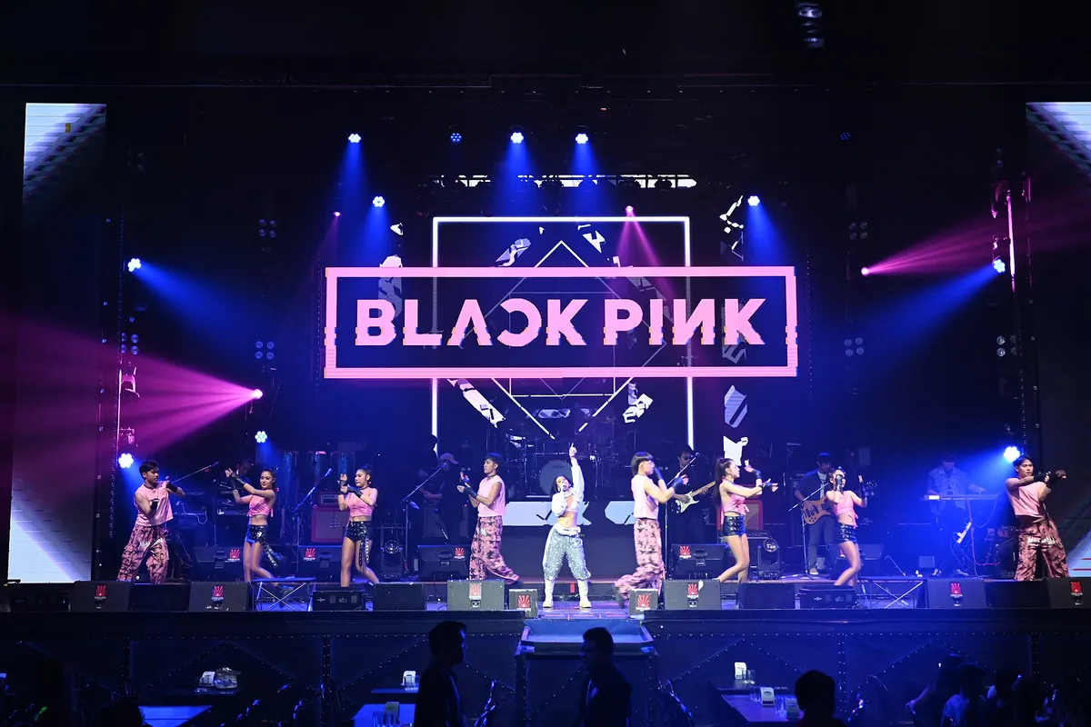 This photo shows a concert performance by BLACKPINK, the popular K-pop girl group. The stage is dramatically lit with blue and purple lighting, and the BLACKPIN
