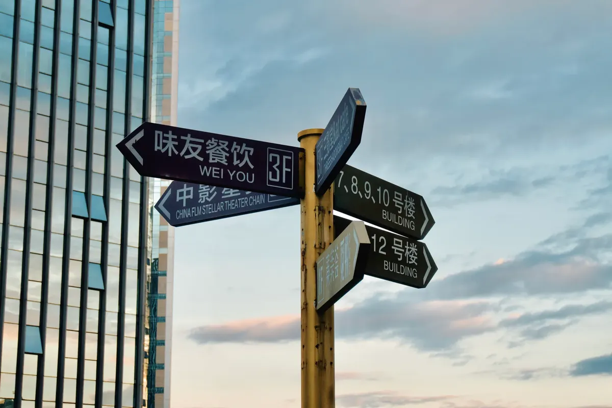 Direction signs in urban area with skyscraper backdrop at sunset.