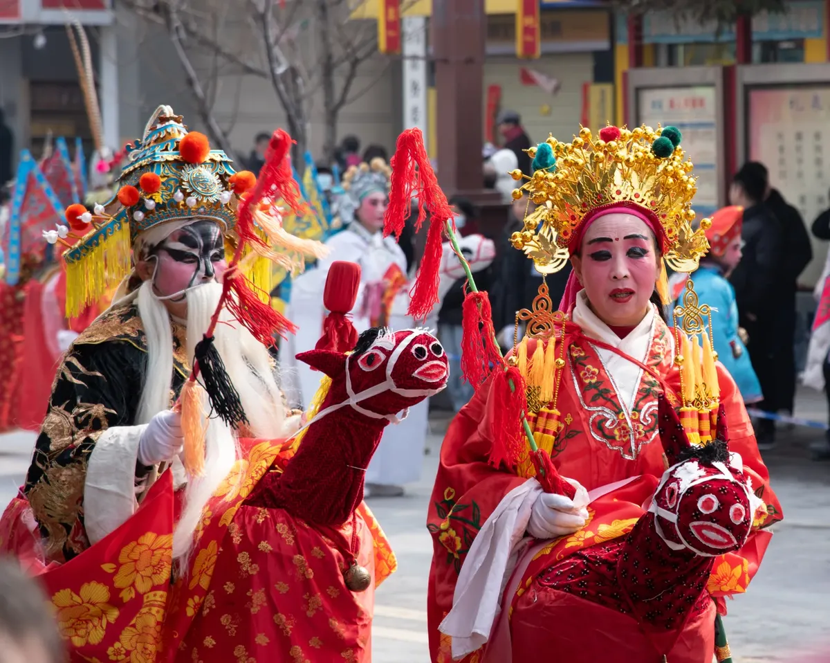 Colorful street parade with performers in traditional costumes and intricate makeup during a cultural festival.