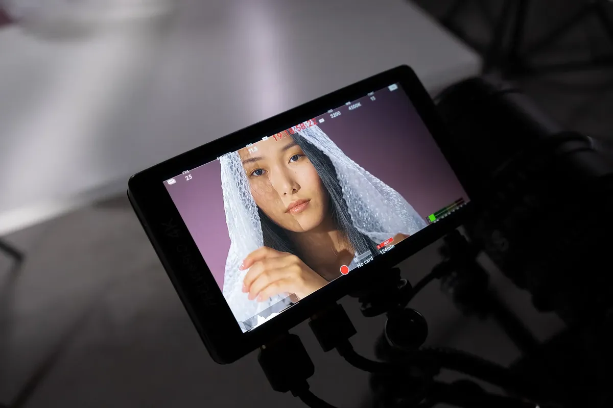 Monitor displays a studio shoot featuring a woman covered in bubble wrap, highlighting behind the scenes.