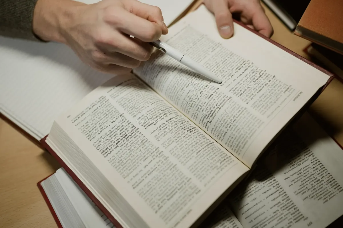 手がペンを握りながら開いた本を読む様子。学習と教育の意図を表す写真。