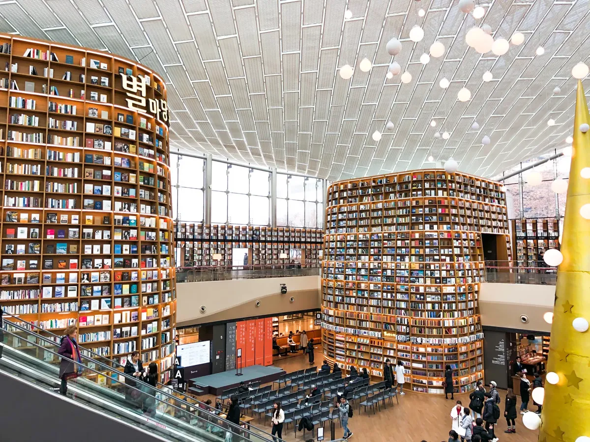 Interior view of a modern South Korean library with towering bookshelves and escalators.